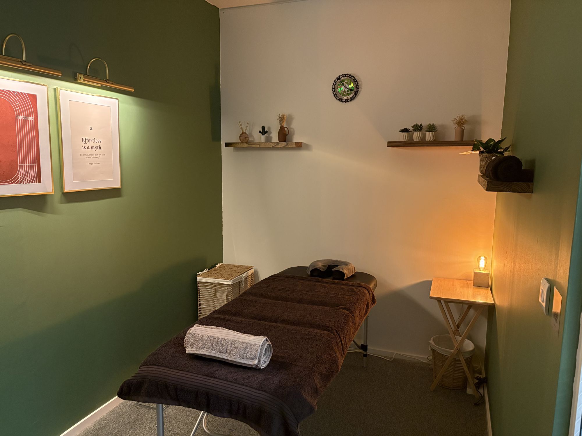The Cairn & Gait treatment room: green walls, brass picture lights, a treatment table made up with brown towels